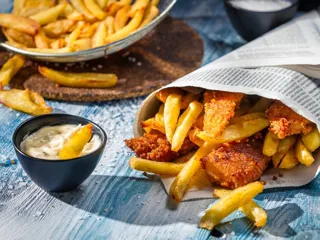 Nærbilde av fish and chips pakket inn i avispapir og dip ved siden av