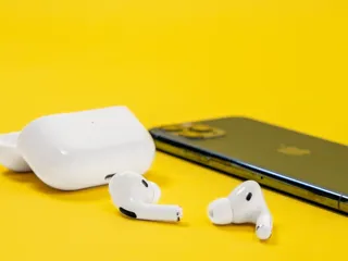 Airpods med etui ligger ved siden av en mobil på gul bakgrunn