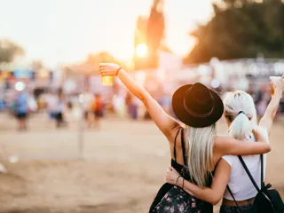 to jenter holder om hverandre og løfter kopper med øl på musikkfestival