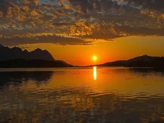 midnattsol reflekterer i vannet med fjellandskap og skyer på himmelen