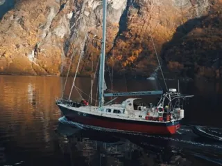 en hvit og rød seilbåt seiler i en fjord