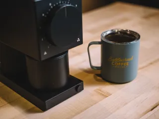 nærbilde av en svart kaffekvern og en kopp kaffe dev siden av