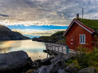 rød hytte med brygge ved en fjord og fjell i bakgrunnen