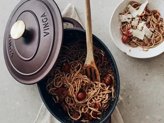 Nærbilde av gryte med lokk med pasta i og tallerken med pasta ved siden av