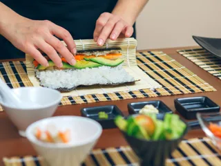 to hender som lager maki rolls med ingredienser i små skåler rundt