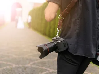 En fotograf med kameraer hengene på skulderen sett bakfra