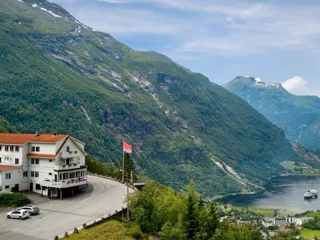 oversiktsbilde av et hvitt hotell som ligger på et fjell med Geirangerfjorden i bakgrunnen