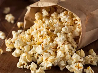 En papipose med popcorn veltet over et trebord med popcornet som faller ut