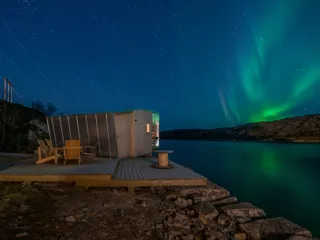 kveldsbilde av en moderne hytte ved sjøen og nordlys på himmelen