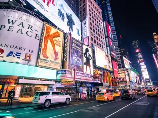 kveldsbilde fra New York med store plakater på fasaden til byggene langs veien