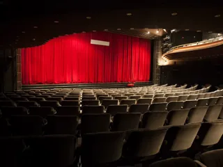 en tom teatersal med røde gardiner som dekker til en stor scene