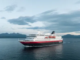 Hurtigruten-skip som seiler med fjell i bakgrunnen